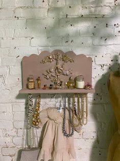 a pink shelf with jewelry on it next to a white brick wall in a room