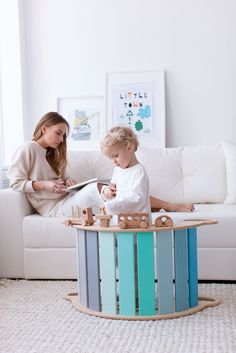 a woman sitting on a couch next to a child playing with a toy train set