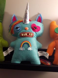 three stuffed animals are on a shelf with one wearing a unicorn hat and the other as a rainbow