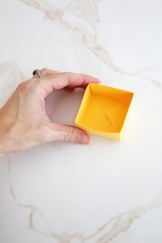 a hand is holding an origami box on a marble surface