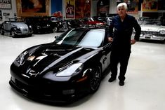 a man standing next to a black sports car in a showroom filled with cars