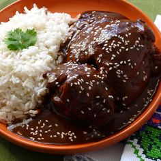 an orange bowl filled with rice and meat covered in gravy on top of a green table cloth