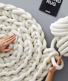 two hands reaching for a large white object made out of interlocked chains on a gray surface