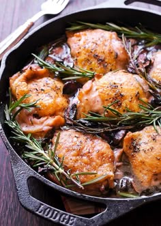 chicken with mushrooms and rosemary in a cast iron skillet on a wooden table next to a fork