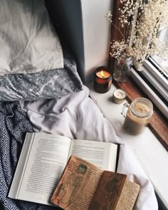 an open book sitting on top of a bed next to a candle and some flowers