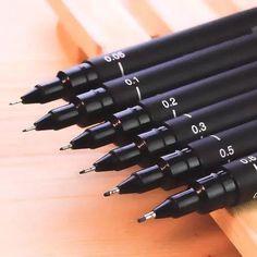 six pens sitting on top of a wooden table