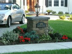 a car is parked in front of a house with flowers around it and a mailbox