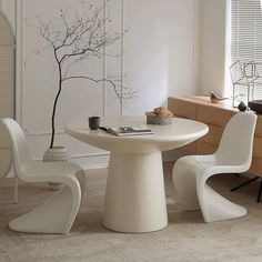 a white table with two chairs and a vase on it in front of a window