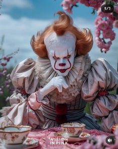 a creepy clown sitting at a table with tea cups and saucers