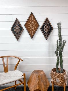 three pieces of art hanging on the wall next to two chairs and a potted cactus