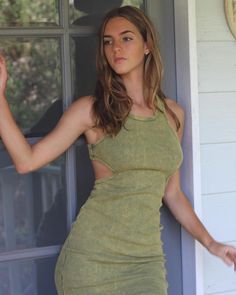 a woman in a green dress leaning against a wall with her hands on her hips