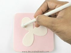 a hand is writing on a piece of paper with a white marker and a pink square