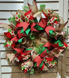 a christmas wreath with red, green and white ribbons hanging on the front door for holiday decor