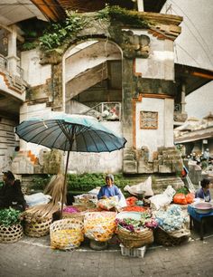 a woman sitting under an umbrella in front of some baskets and vegetables on the ground