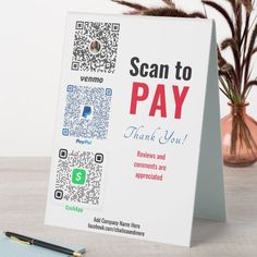 a sign that says scan to pay on it next to a pen and potted plant