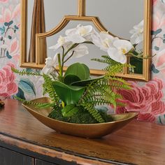 a bowl filled with white flowers on top of a wooden table next to a mirror