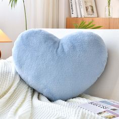 a blue heart shaped pillow sitting on top of a white couch next to a lamp