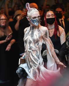 a model walks down the runway wearing an unusual mask and dress with feathers on it