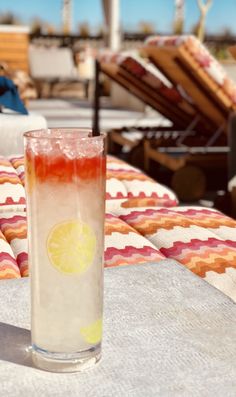 a glass filled with liquid sitting on top of a table next to a beach chair