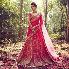 a woman in a pink lehenga standing in the woods with her hands on her hips