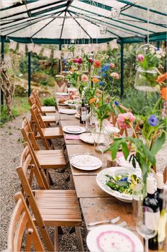 a long wooden table with plates and flowers in vases on it under a tent