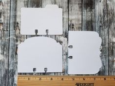 three pieces of white paper sitting on top of a wooden table next to a ruler