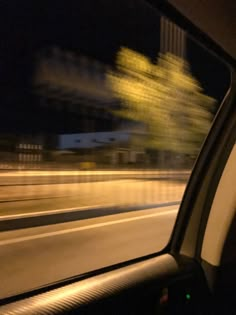 the view from inside a car at night with blurry trees and buildings in the background