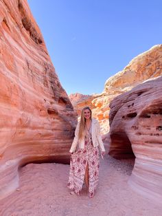 a woman is standing in the middle of a narrow slot with red rock formations behind her