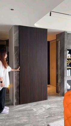 a woman standing in front of a mirror next to an orange chair and black wall