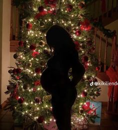 the silhouette of a pregnant woman in front of a christmas tree with lights on it