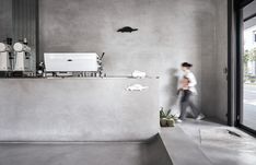 a man walking past a bathroom sink next to a wall with mirrors and sinks on it