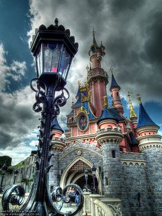 a street light sitting in front of a castle under a cloudy sky with dark clouds