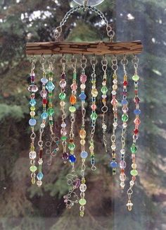 a wind chime hanging from a window in front of a pine tree filled with lots of beads