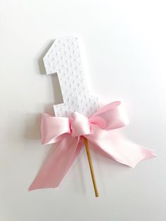 a pink bow on top of a white number one stick with the letter e in it