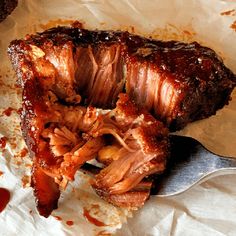 a piece of meat with sauce on it and a fork next to it sitting on wax paper