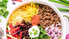 a large bowl filled with taco salad and toppings next to cilantro