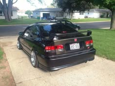 the back end of a black car parked in front of a house on a sidewalk