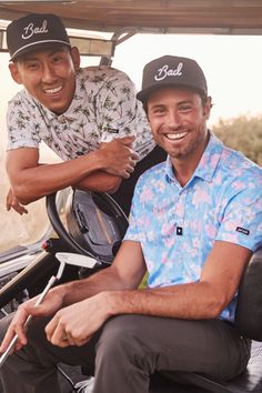 two men sitting on the back of a golf cart smiling at the camera while another man stands next to them