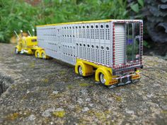 a toy truck is sitting on top of a rock in front of some grass and bushes