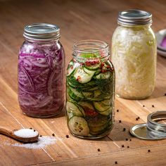 three mason jars filled with pickles, onions and cucumbers on a wooden table