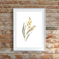 a white frame hanging on a brick wall next to a plant with yellow flowers in it