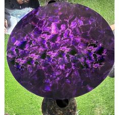 a purple marble table sitting on top of a grass covered field next to a man