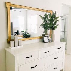 a white dresser topped with a mirror and a potted plant