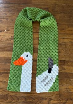 a green knitted scarf with a white duck on the front and an orange beak on the back