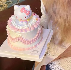 a hello kitty cake sitting on top of a white box next to a woman's head