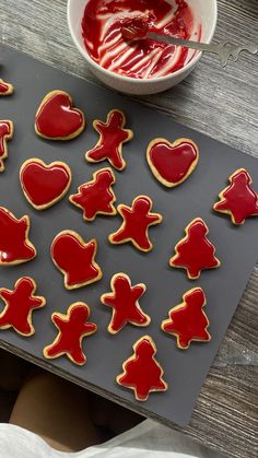 the cookies are decorated with red icing and heart shapes on a cookie sheet next to a bowl of jelly