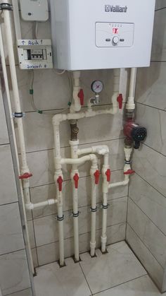 a white tank mounted to the side of a wall next to pipes and piping