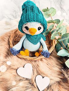 a knitted penguin sitting in a basket next to two hearts on a fur rug