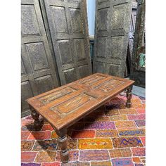 an old wooden coffee table sitting on top of a colorful tile floor next to two large doors