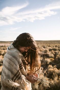 a woman with long hair wrapped in a blanket is standing in the middle of an open field